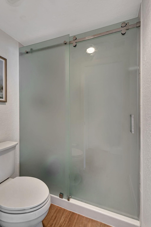 bathroom featuring wood-type flooring, an enclosed shower, and toilet