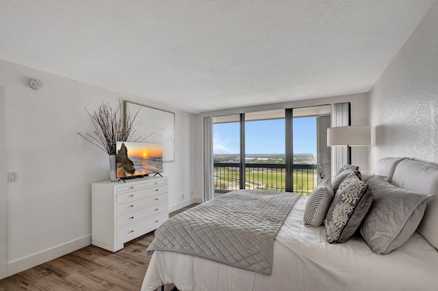 bedroom featuring expansive windows, wood-type flooring, a textured ceiling, and access to outside