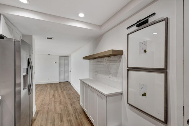 kitchen featuring stainless steel fridge with ice dispenser, light hardwood / wood-style flooring, white cabinetry, and tasteful backsplash