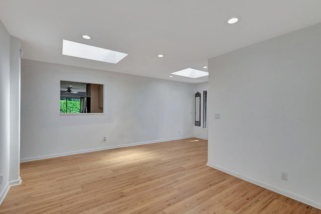 unfurnished room with a skylight, ceiling fan, and light wood-type flooring