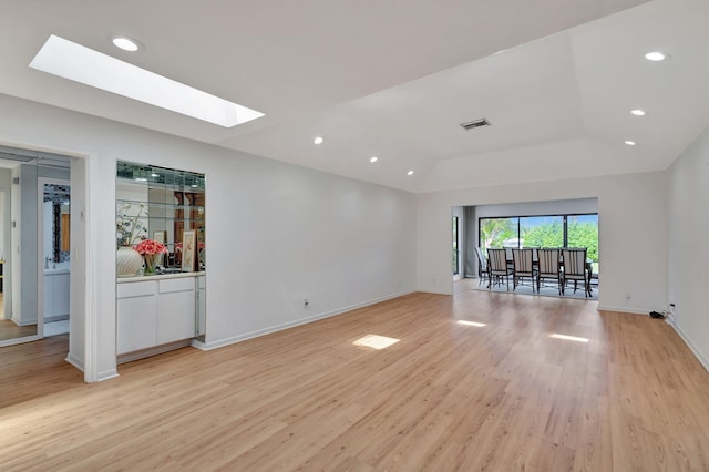 spare room with a skylight, light hardwood / wood-style flooring, and a raised ceiling