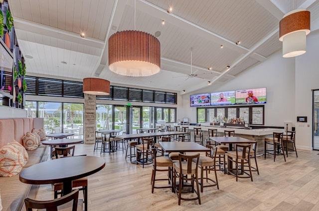 dining space with high vaulted ceiling, ceiling fan, and light hardwood / wood-style flooring