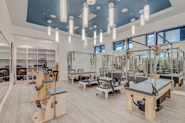 exercise room with light hardwood / wood-style floors, a high ceiling, a tray ceiling, and a healthy amount of sunlight