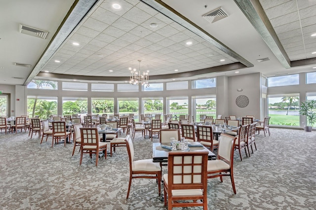 dining space with carpet floors, a high ceiling, an inviting chandelier, and a raised ceiling