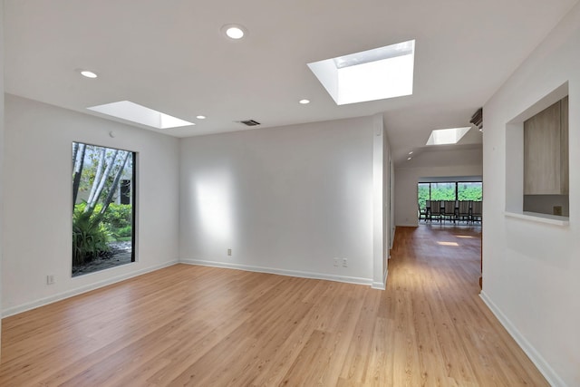 empty room with a skylight, light hardwood / wood-style flooring, and a wealth of natural light