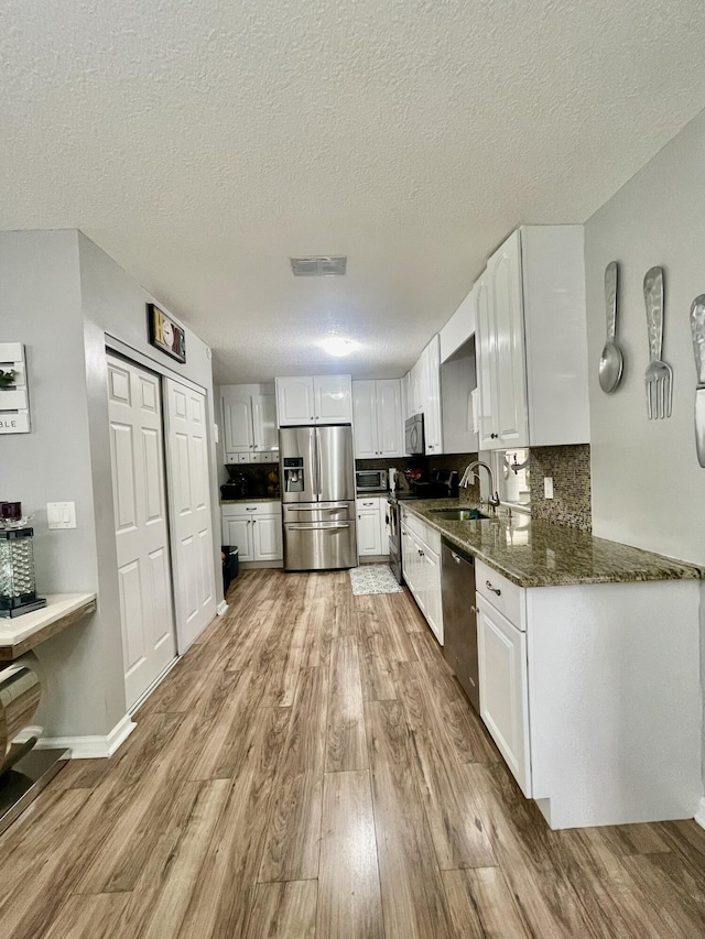 kitchen with appliances with stainless steel finishes, dark stone counters, a textured ceiling, white cabinets, and light wood-type flooring