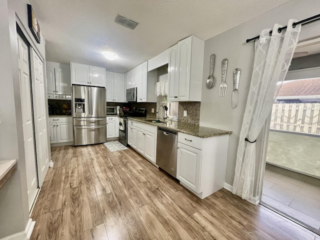 kitchen featuring dark stone countertops, white cabinetry, stainless steel appliances, and light hardwood / wood-style floors