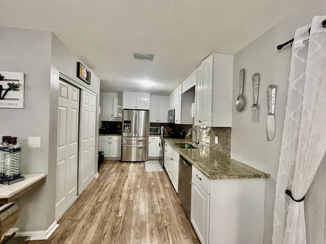 kitchen featuring appliances with stainless steel finishes, tasteful backsplash, sink, light hardwood / wood-style floors, and white cabinetry