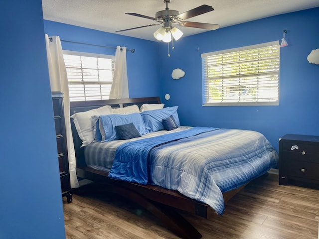 bedroom with ceiling fan, wood-type flooring, a textured ceiling, and multiple windows