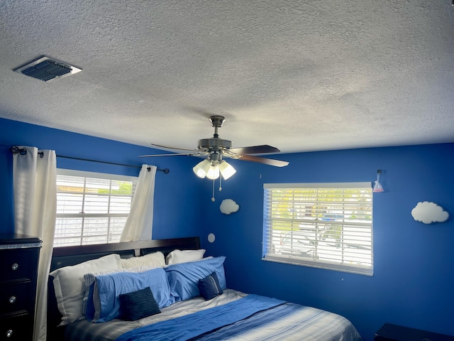 bedroom featuring ceiling fan, a textured ceiling, and multiple windows