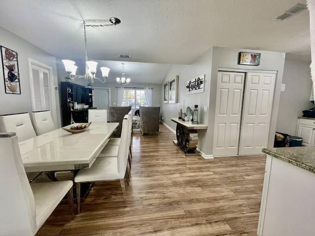 dining room featuring a textured ceiling, lofted ceiling, light hardwood / wood-style flooring, and an inviting chandelier