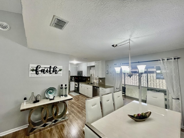 dining room featuring hardwood / wood-style floors, a notable chandelier, sink, and a textured ceiling