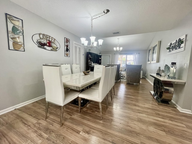 dining space featuring hardwood / wood-style floors, a textured ceiling, an inviting chandelier, and lofted ceiling