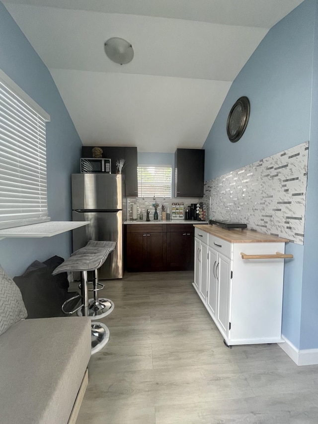 kitchen featuring appliances with stainless steel finishes, light wood-type flooring, backsplash, vaulted ceiling, and butcher block countertops