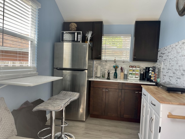 kitchen featuring sink, decorative backsplash, light wood-type flooring, butcher block countertops, and stainless steel refrigerator