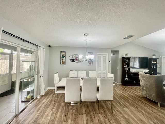 dining room with a textured ceiling, an inviting chandelier, lofted ceiling, and hardwood / wood-style flooring