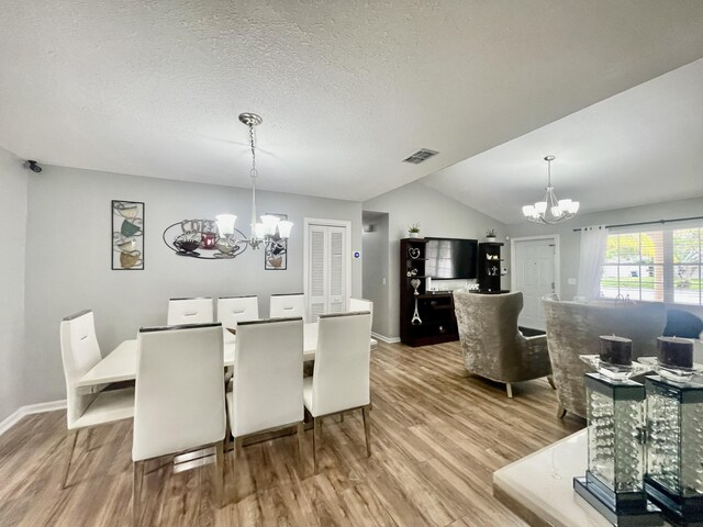 dining space featuring a textured ceiling, wood-type flooring, lofted ceiling, and an inviting chandelier