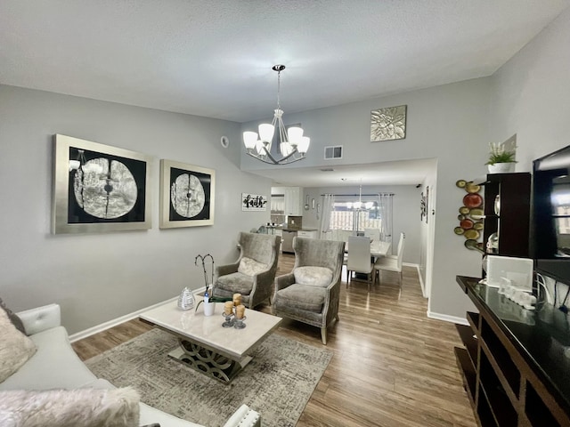 living room with hardwood / wood-style flooring, vaulted ceiling, a textured ceiling, and an inviting chandelier