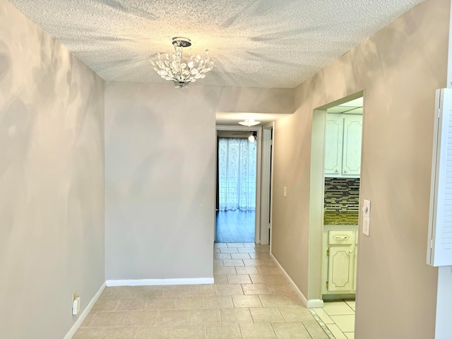 corridor featuring a textured ceiling, light tile patterned floors, and an inviting chandelier