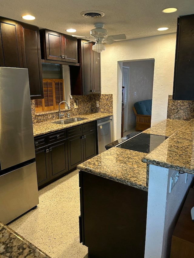 kitchen featuring dark brown cabinetry, sink, stainless steel appliances, backsplash, and dark stone counters