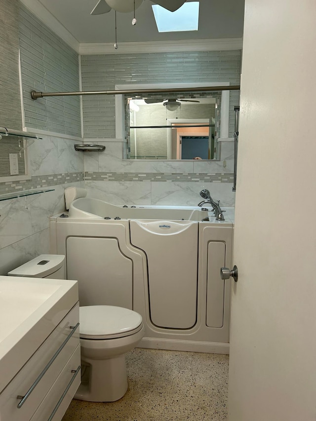 bathroom featuring a skylight, a bathtub, vanity, tile walls, and ornamental molding