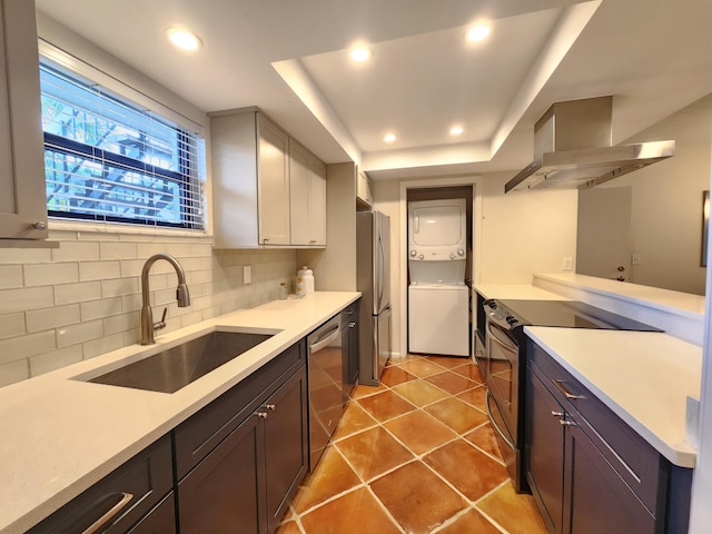 kitchen featuring sink, wall chimney exhaust hood, decorative backsplash, stacked washer and clothes dryer, and appliances with stainless steel finishes