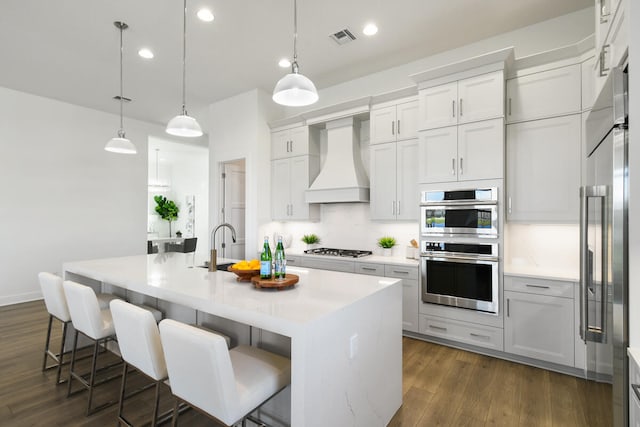 kitchen featuring custom exhaust hood, white cabinetry, a kitchen island with sink, dark wood-type flooring, and pendant lighting