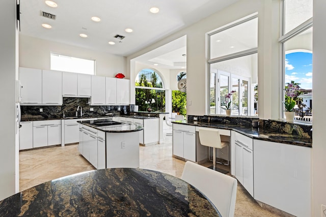 kitchen featuring cooktop, dark stone countertops, white cabinetry, and a center island