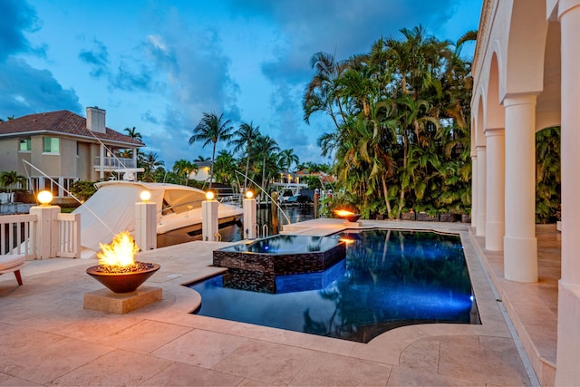 pool at dusk featuring a fire pit, a patio area, and an in ground hot tub