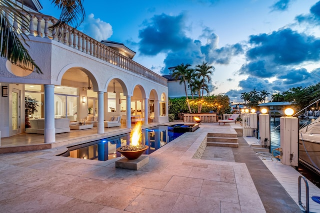 patio terrace at dusk featuring a balcony, an outdoor living space with a fire pit, and a pool with hot tub