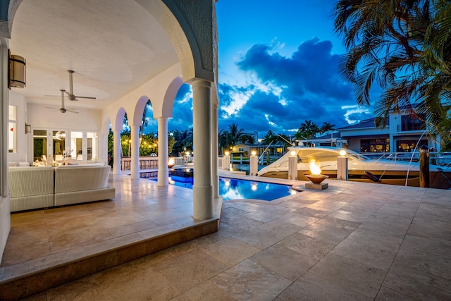 pool at dusk with ceiling fan, a patio area, and a boat dock