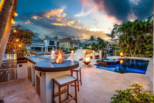 pool at dusk featuring a bar, a patio, a fire pit, and grilling area