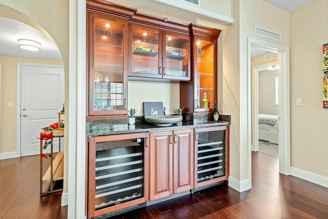 bar featuring dark hardwood / wood-style flooring, beverage cooler, and dark stone counters