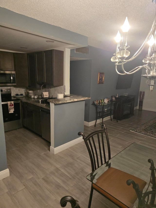 kitchen with stainless steel appliances, kitchen peninsula, dark stone counters, a textured ceiling, and dark brown cabinets