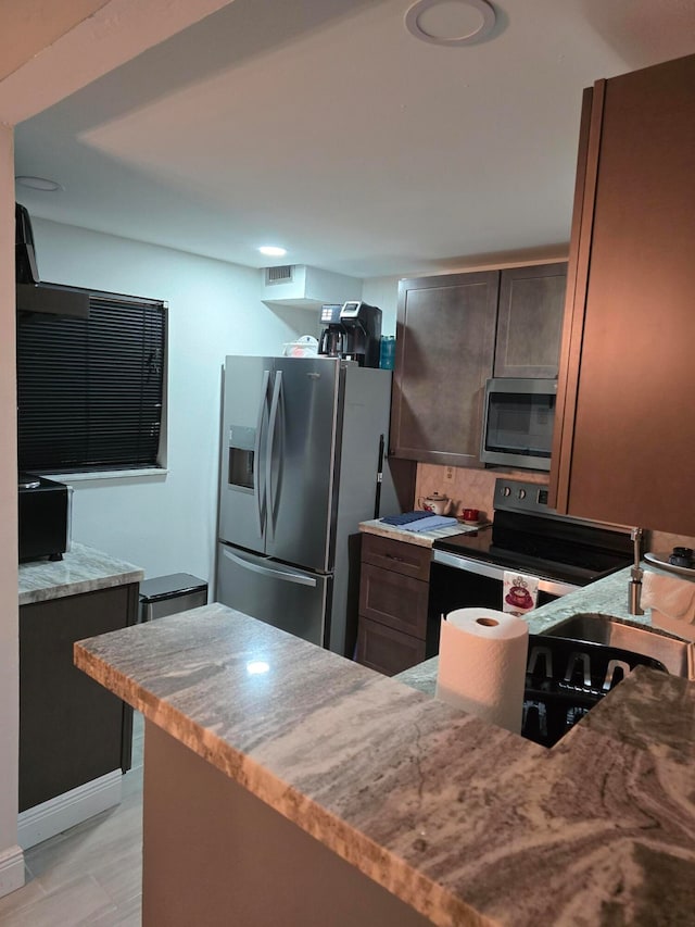 kitchen featuring decorative backsplash, appliances with stainless steel finishes, light wood-type flooring, dark brown cabinets, and sink