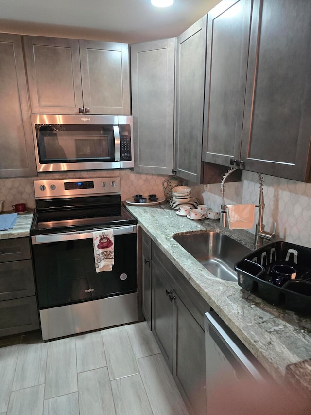 kitchen featuring decorative backsplash, appliances with stainless steel finishes, light stone countertops, dark brown cabinetry, and sink