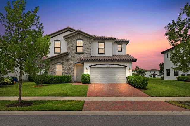 mediterranean / spanish-style home with stucco siding, a lawn, decorative driveway, stone siding, and a tiled roof