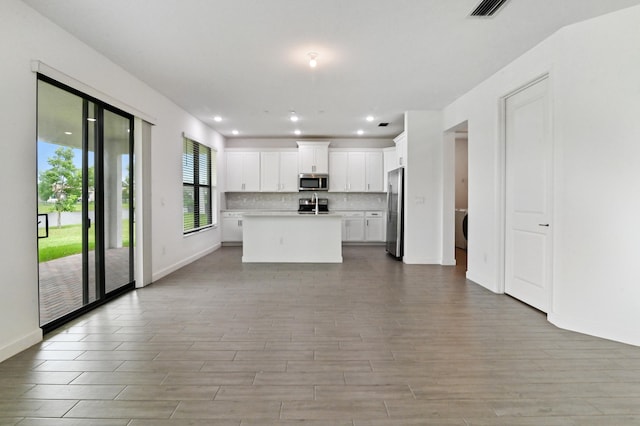 kitchen with an island with sink, tasteful backsplash, white cabinets, stainless steel appliances, and light hardwood / wood-style flooring