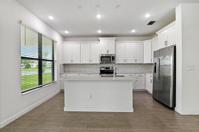 kitchen with stainless steel appliances, white cabinets, a kitchen island with sink, and sink