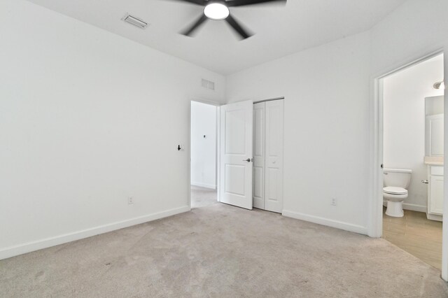 unfurnished bedroom featuring light carpet, connected bathroom, a closet, and ceiling fan