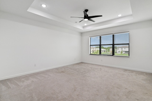 carpeted empty room featuring ceiling fan and a raised ceiling