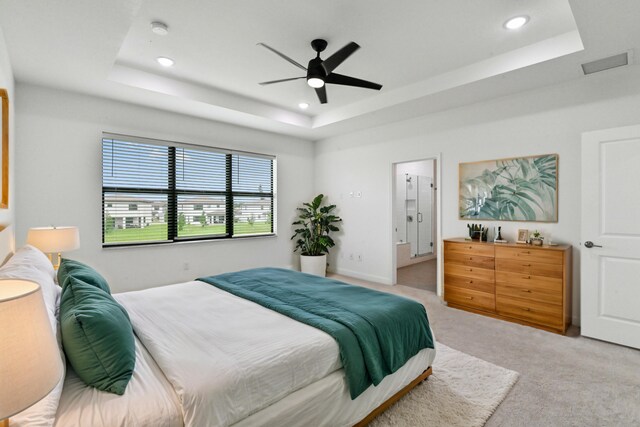 bedroom featuring light carpet, a tray ceiling, and ceiling fan