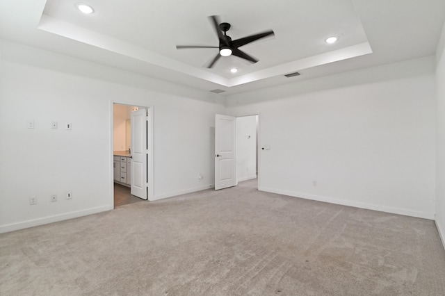 unfurnished bedroom with a raised ceiling, carpet flooring, ensuite bath, and ceiling fan