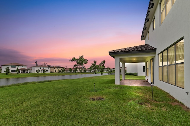 yard at dusk featuring a patio and a water view