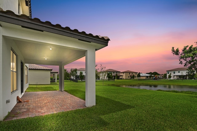 yard at dusk with a water view and a patio area