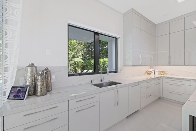 kitchen featuring decorative backsplash, light stone countertops, sink, and white cabinets