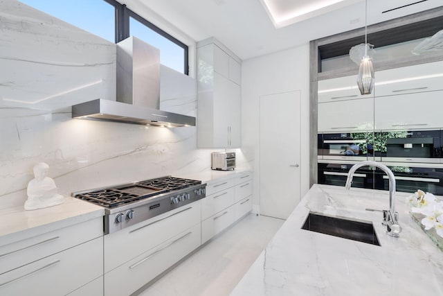 kitchen with pendant lighting, white cabinets, wall chimney range hood, sink, and tasteful backsplash