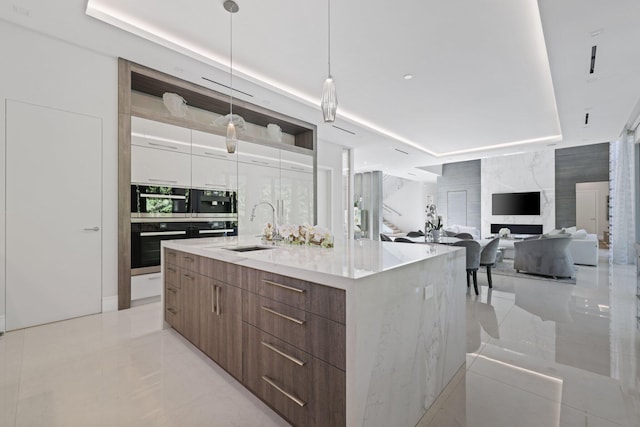 kitchen featuring sink, decorative light fixtures, tile walls, white cabinets, and a large island