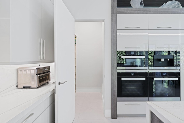 kitchen featuring light tile patterned floors, light stone countertops, white cabinetry, and double oven