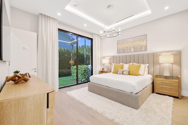 bedroom featuring a tray ceiling, access to exterior, a notable chandelier, and light wood-type flooring